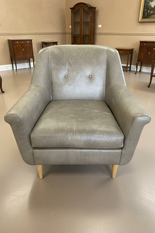 Beige leather armchair in a storage or warehouse setting with various items in the background.